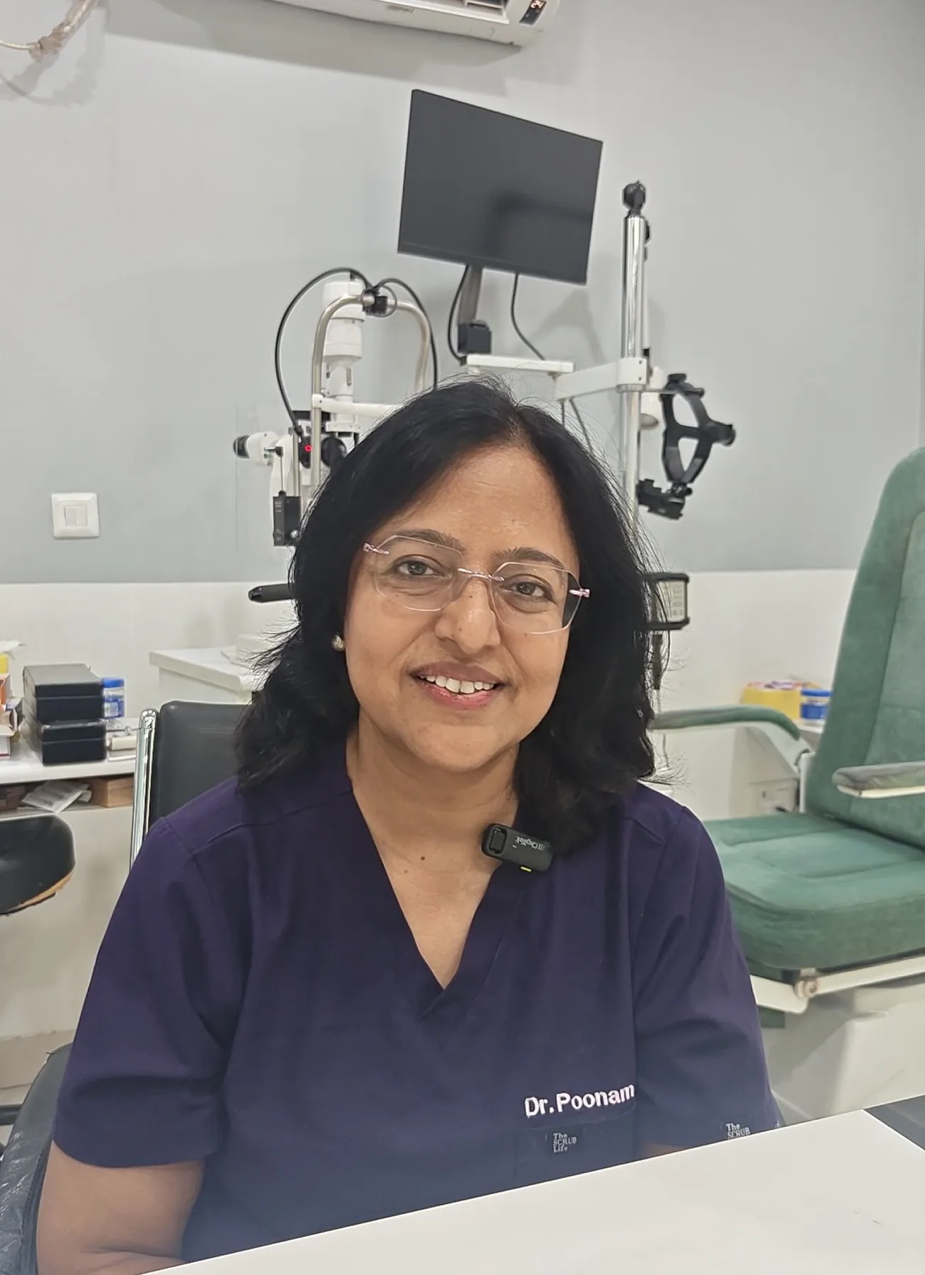 Dr. Poonam Jain smiling, seated at her desk in navy scrubs