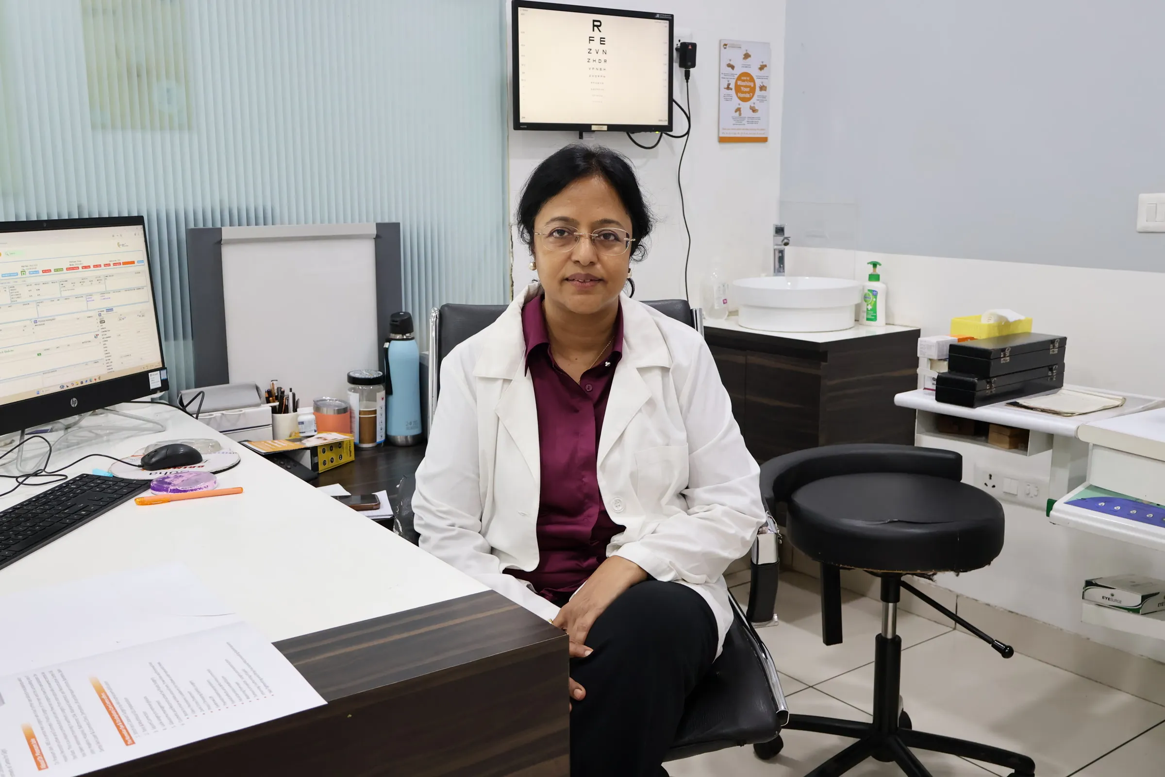 Dr. Poonam Jain seated at her consultation desk, with a computer and a slit-lamp unit behind