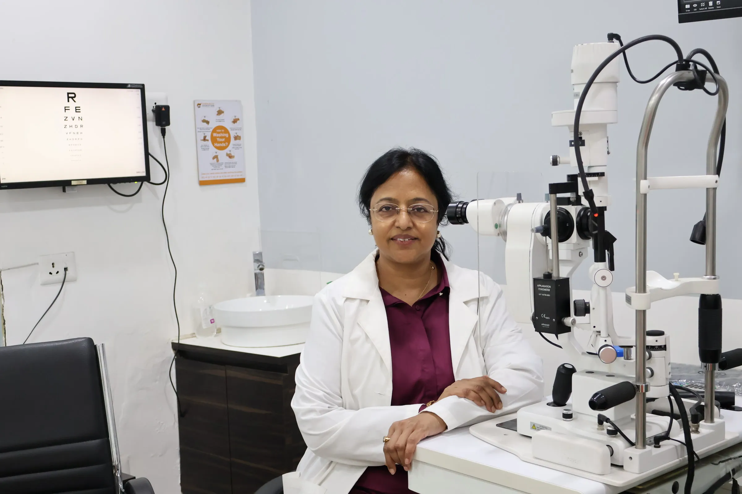 Dr. Poonam Jain seated beside a slit-lamp examination unit in a consultation room