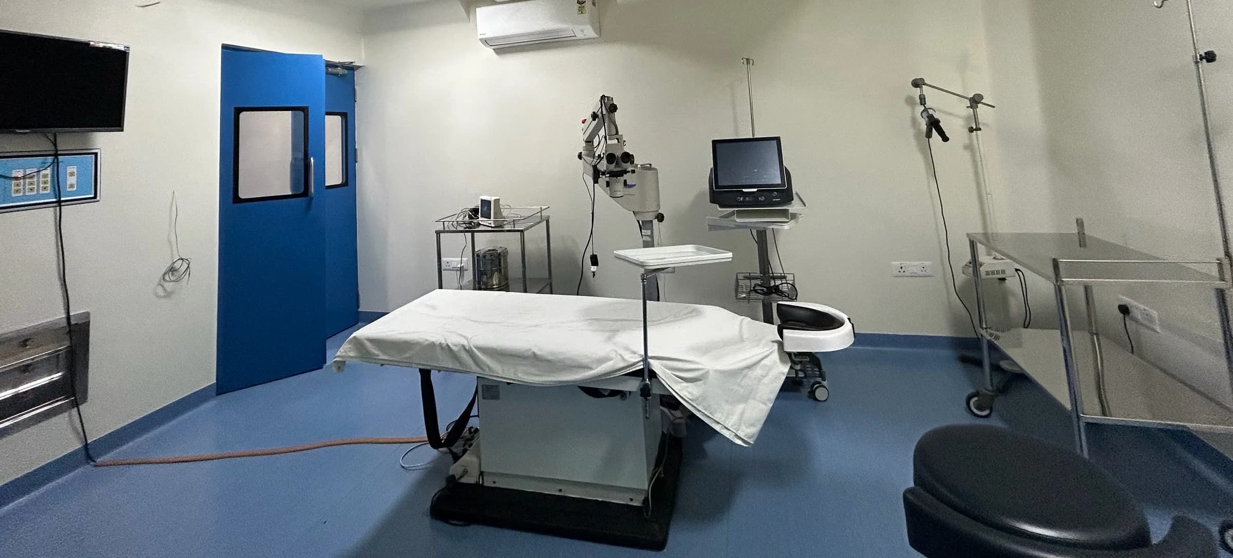 The same operation theatre from the door side, showing the operating table, operating microscope and a console on a stand